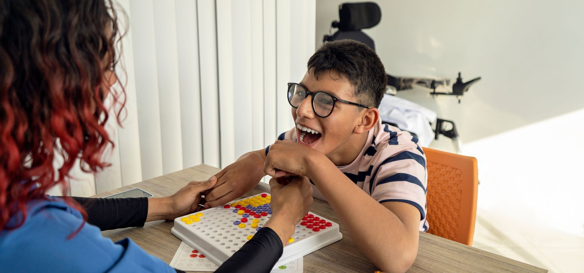 Child with glasses smiling and playing a game during a therapy session, reflecting joy and engagement in a supportive environment