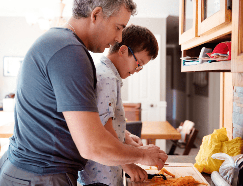 A young adult being assisted by a caregiver in a kitchen, preparing a meal together at Concept Care Community Services.