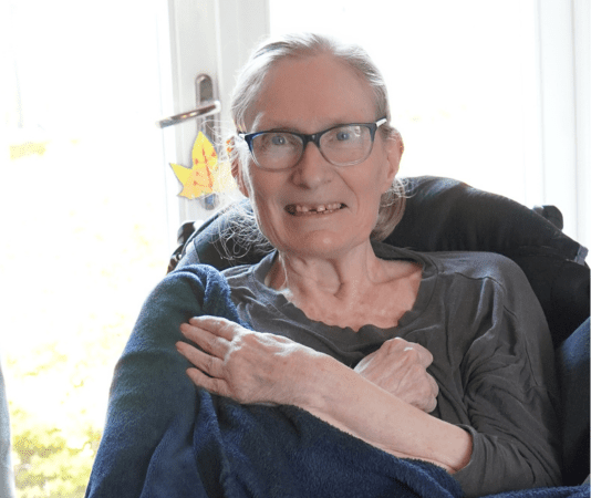 Elderly woman smiling while holding a cat, representing companionship and care.