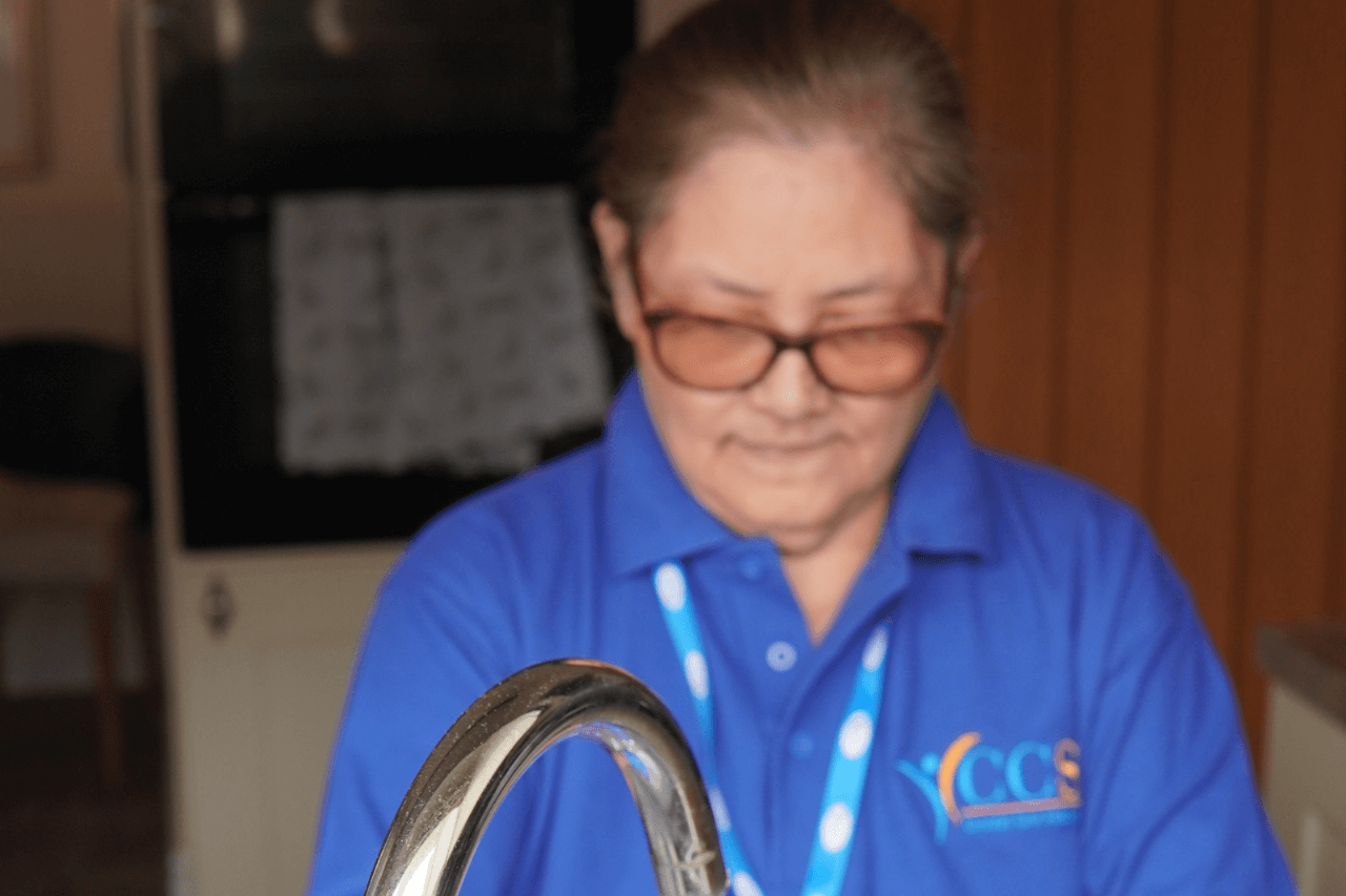 A caregiver from Concept Care Community Services wearing a blue uniform and glasses, smiling while attending to a task.