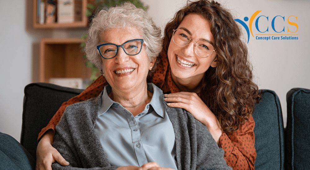 A joyful elderly woman sitting with a younger family member, both smiling, symbolising the importance of family caregivers in providing emotional support and care.